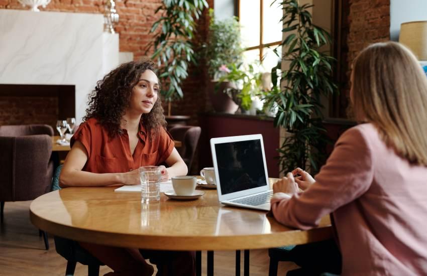 two women talking over coffee and a laptop