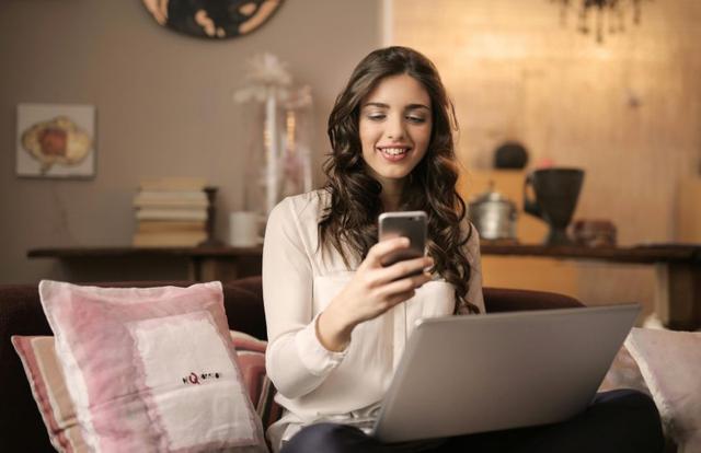 Woman smiling at her phone on a laptop
