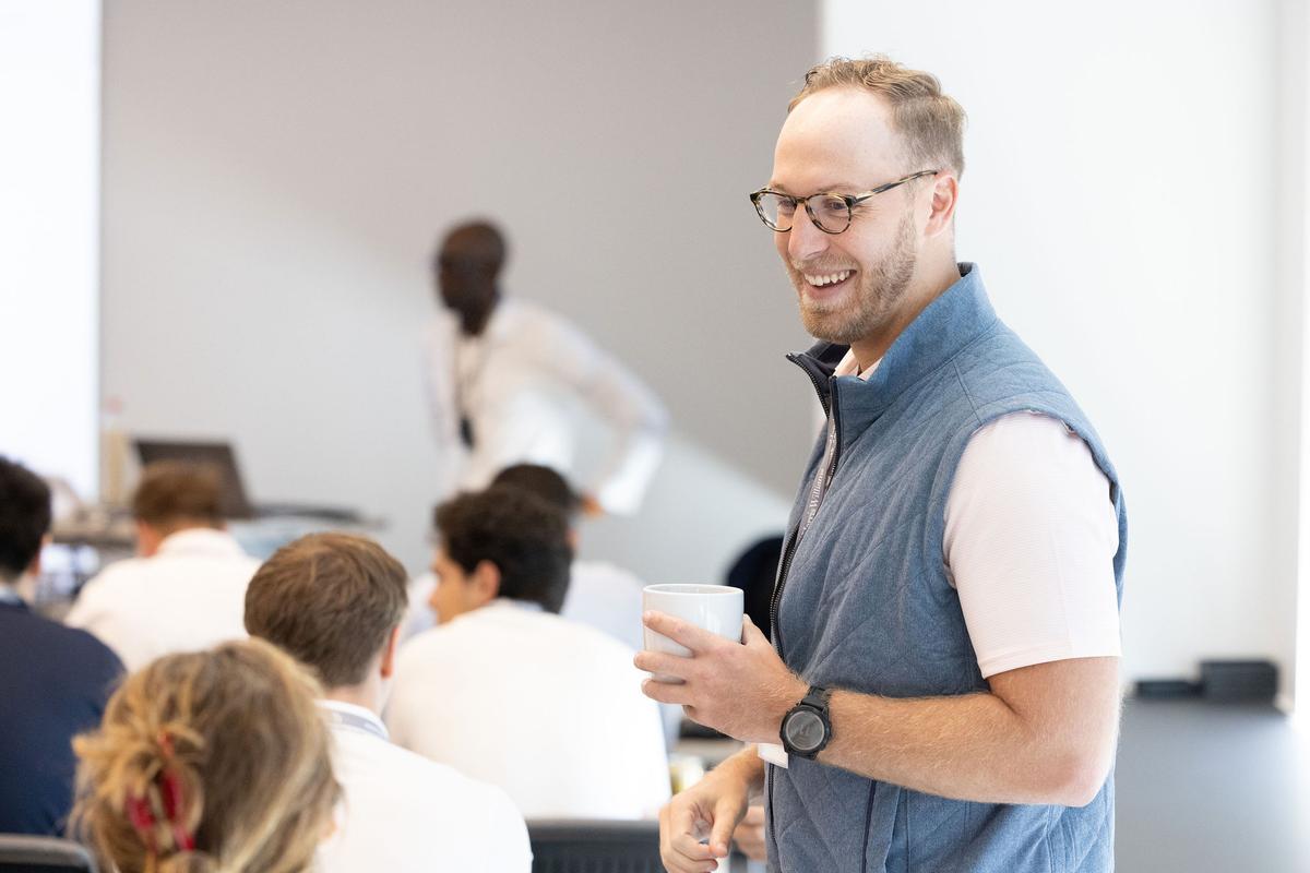 man with coffee talking to a coworker at a presentation