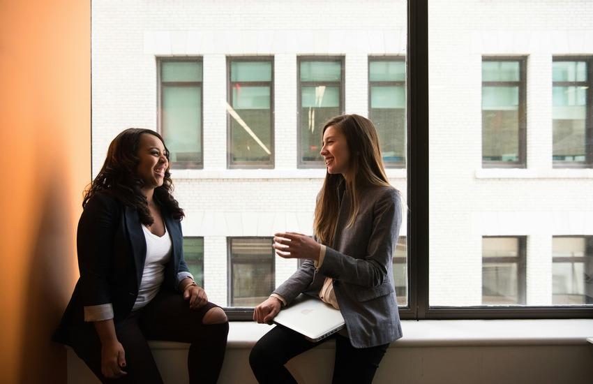 two coworkers sitting on a windowsill and chatting
